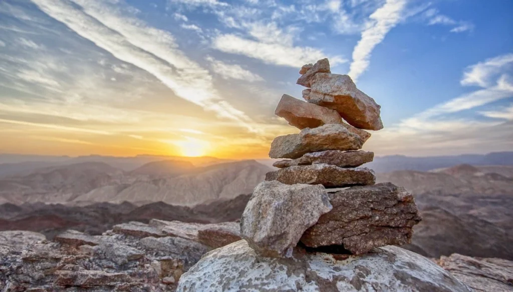 A pile of rocks at the top of a mountain with the sun going down